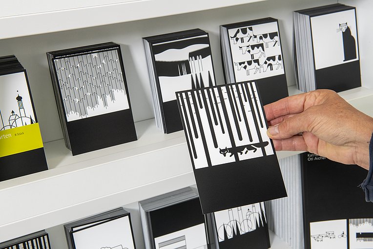 Hand häft eine schwarz-weiße Postkarte mit einem Fuchs darauf, im Hintergrund mehr Postkarten