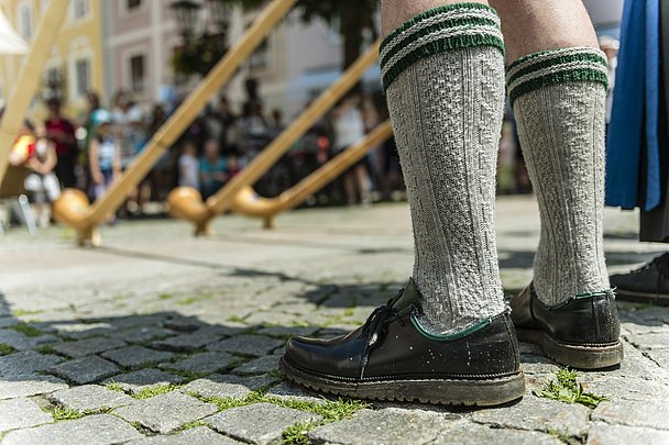 Füße eines Alphornbläsers in Haferlschuhen und traditionellen Socken, im Hintergrund Alphörner