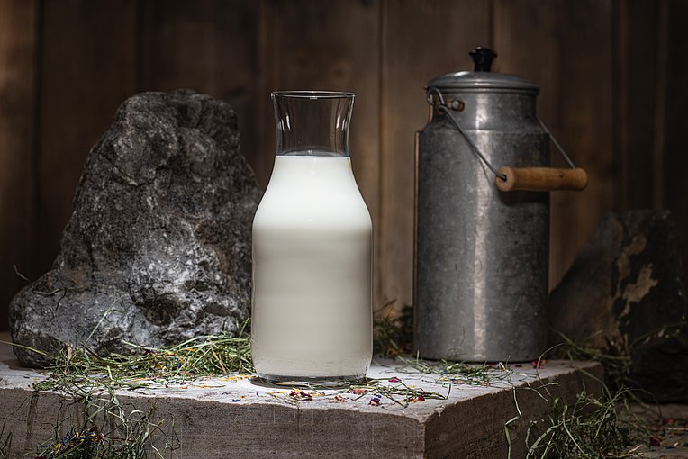 Heumilch in der Glasflasche mit alter Milchkanne