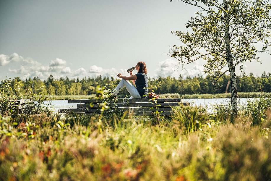 Frau trinkt aus einer Wasserflasche bei einer Pause an einem See