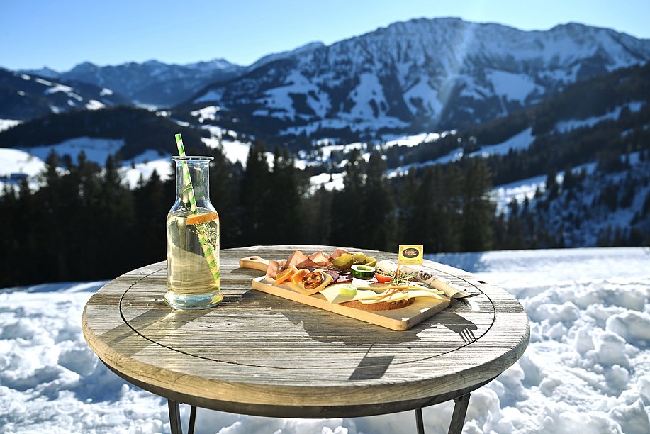 Brotzeit und hausgemachte Limo auf einem Tisch auf der Buchel Alpe vor verschneiten Bergen Brotzeit und hausgemachte Limo auf einem Tisch auf der Buchel Alpe vor verschneiten Bergen