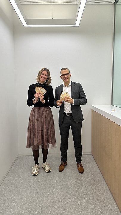 JobQuesterin Pia und ein Angestellter der Sparkasse mit Geldscheinen in der Hand