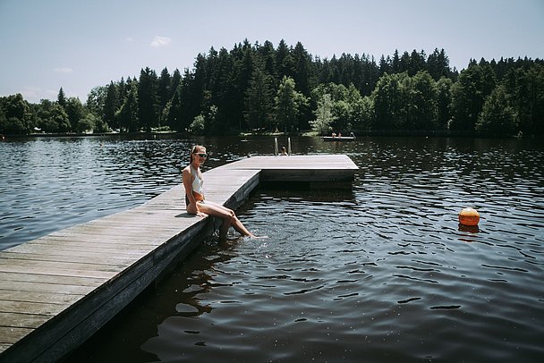 Frau sitzt auf einem Holzsteg in Lindenberger Waldsee
