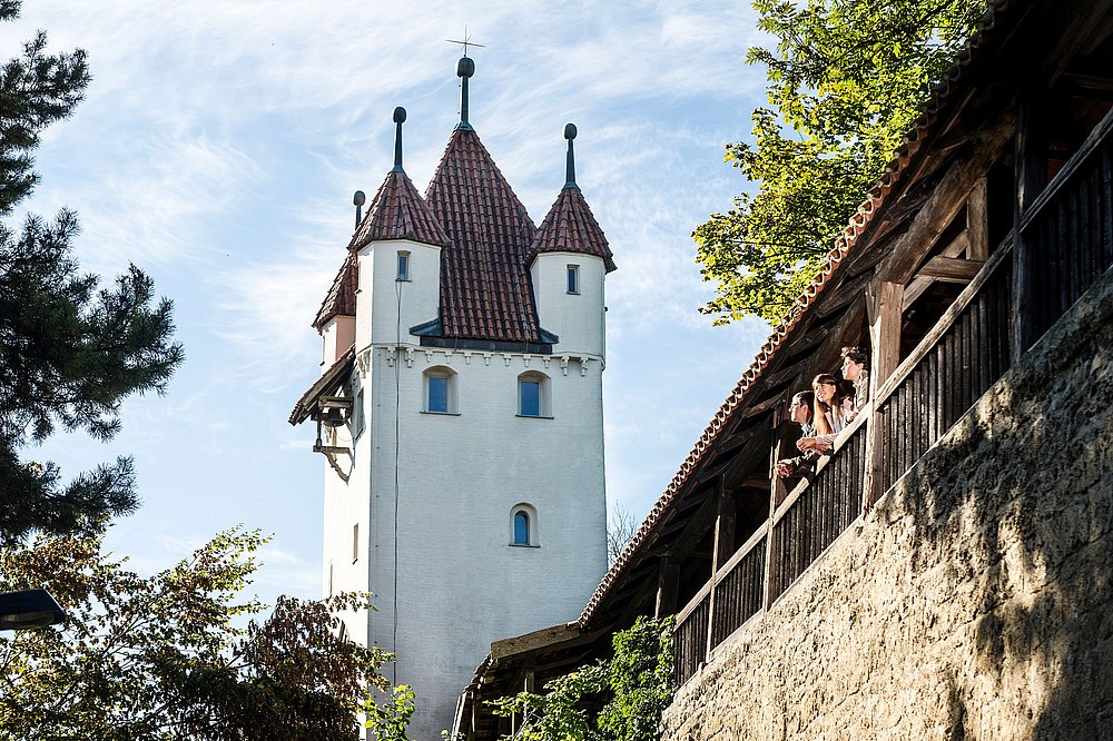Fünfknopfturm in Kaufbeuren, davor die Stadtmauer, aus deren Wehrgang drei Personen schauen