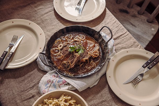 Eine Pfanne mit Zwiebelfleisch, drei Teller und Besteck