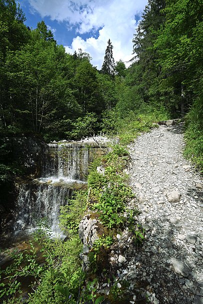 Wanderweg neben einem Wasserfall über zwei künstliche Steinstufen