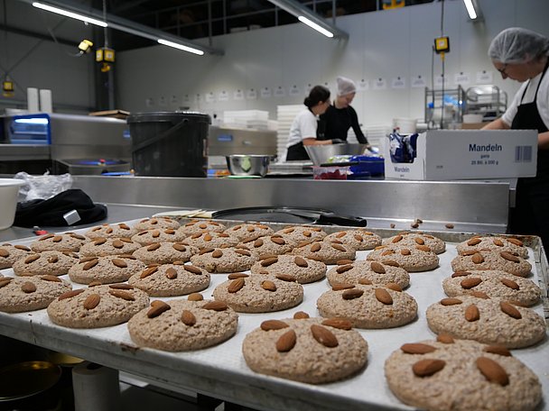 Blech mit ungebackenen Lebkuchen, im Hintergrund Frauen bei der Arbeit
