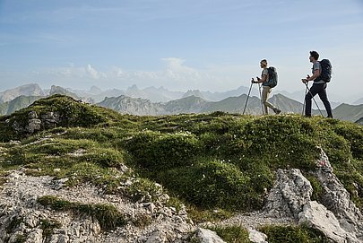 Zwei Wanderer auf einem Bergwanderweg vor Alpenpanorama