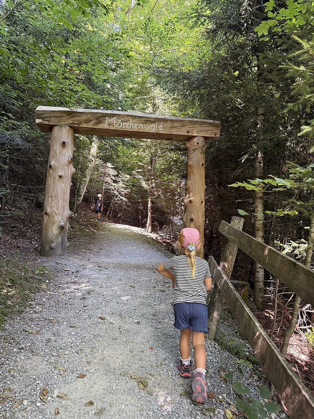 Mädchen auf einem Waldweg, läuft auf ein Holztor mit der Aufschrift "Märchenwald" zu