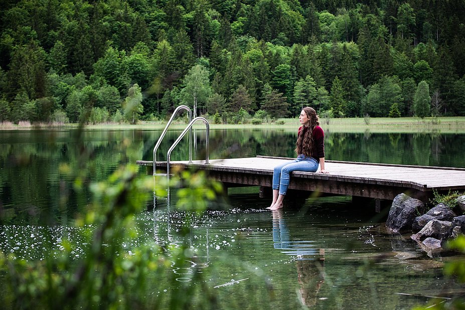 Frau auf einem Steg am Schwansee, Füße im Wasser