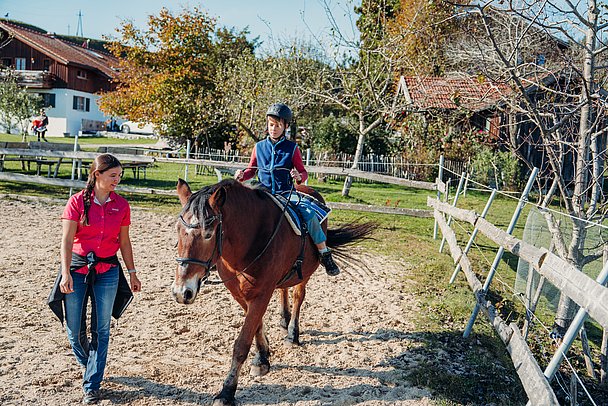 Kind reitet auf einem Reitplatz im Freien mit Reitlehrerin 