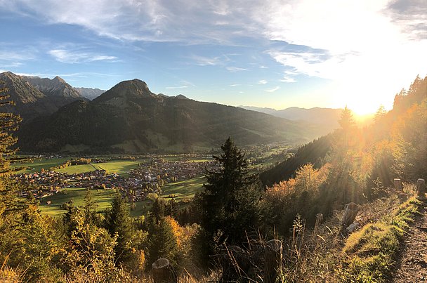 Blick von Wanderweg über Bad Hindelang und die Berge im Licht der untergehenden Sonne