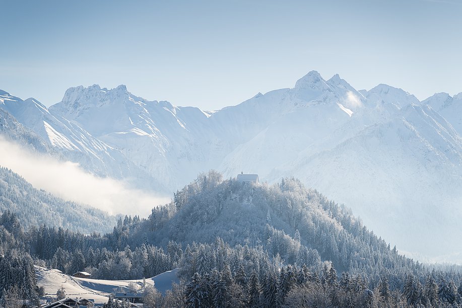Schöllanger Burgkirche auf einem bewaldeten Hügel, verschneite Landschaft mit Bergen Schöllanger Burgkirche auf einem bewaldeten Hügel, verschneite Landschaft mit Bergen