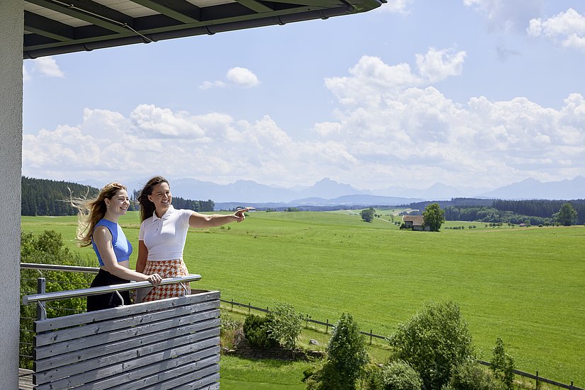 Zwei Frauen auf einem Balkon, im Hintergrund Wiesen und Berge