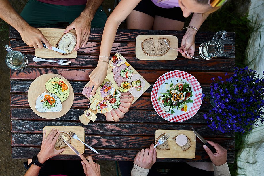 Ein Tisch mit Brotzeit von oben, vier Menschen essen