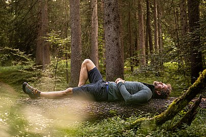 Mann liegt auf einem liegenden Baumstamm im Wald
