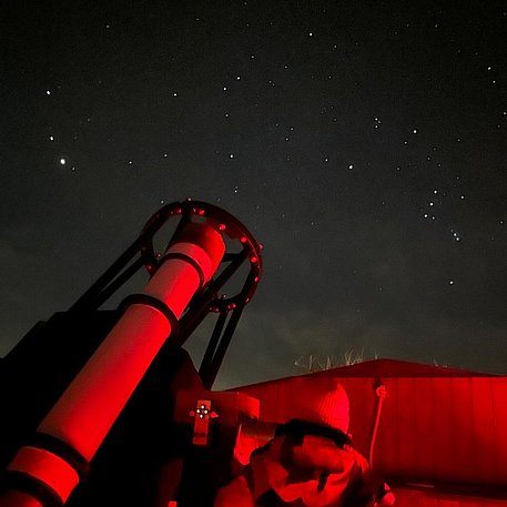 Junge neben einem Teleskop vor Sternenhimmel