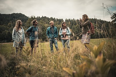 Naturführerin steht mit einer Gruppe auf einer Wiese und erklärt etwas