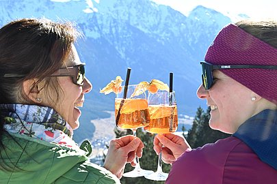 Zwei Frauen stoßen mit Aperol an, im Hintergrund die verschneiten Hindelanger Berge
