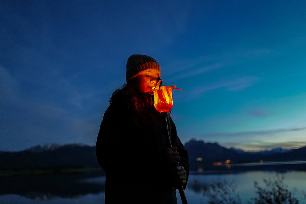 Ein Mädchen guckt in der Dämmerung in ihre selbstgebastelte, leuchtende Fackel, ihr Gesicht wird erhellt