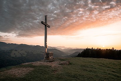 Gipfelkreuz und Berge im Licht der untergehenden Sonne