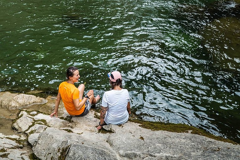 Zwei Frauen sitzen auf den Felsen vor dem Becken an den Buchenegger Wasserfällen