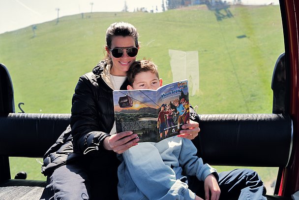 Mutter und Sohn lesen das MounTeens-Rästelheft in der Gondel