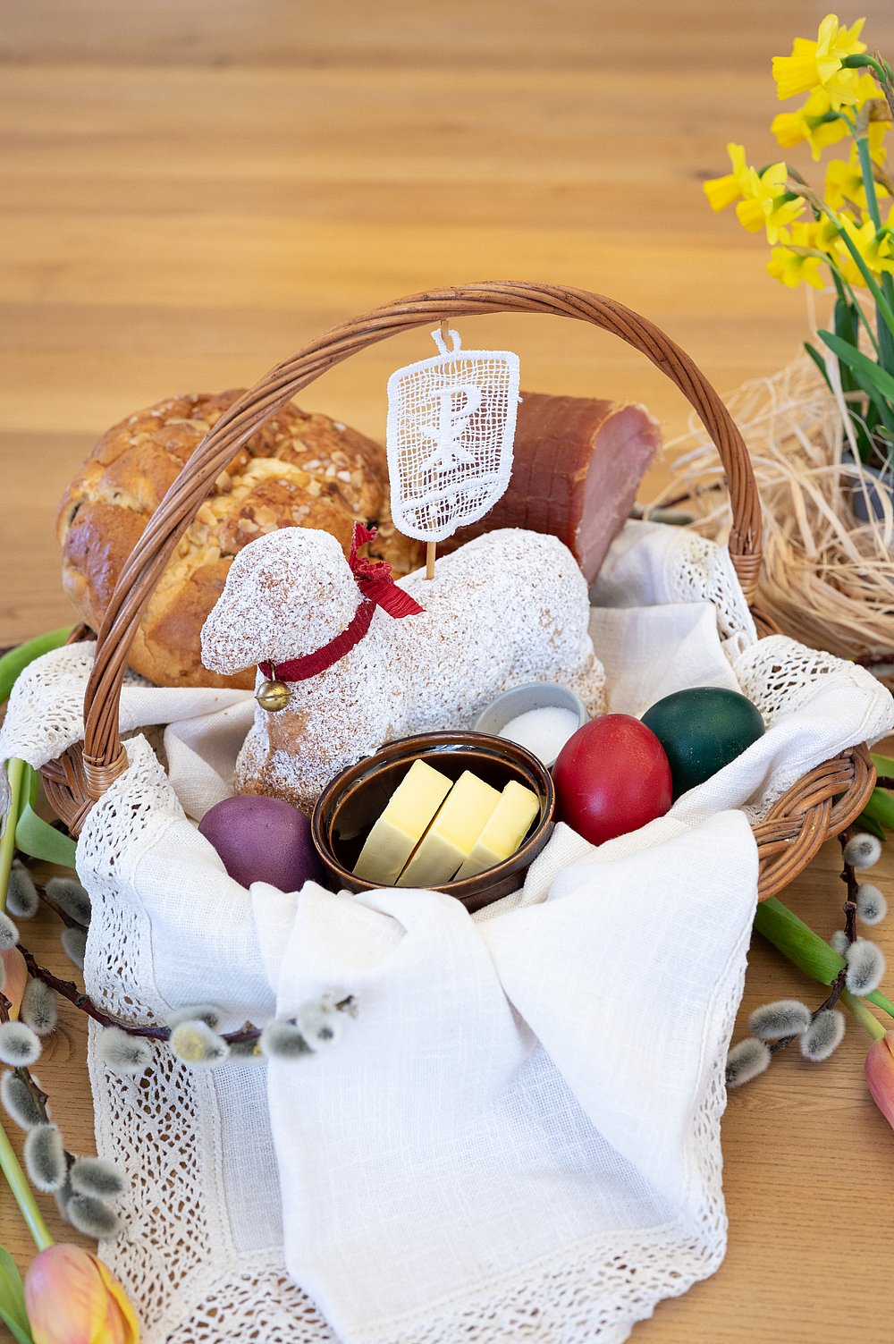 Osterkorb mit gebackenem Osterlamm, bunten Eiern, Butter, Salz, Osterbrot und Schinken