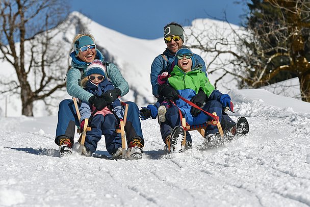 Eltern mit drei Kindern beim Rodeln