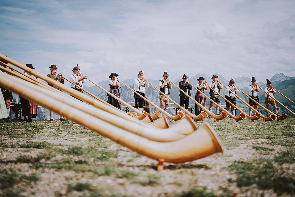 Männer und Frauen in Tracht spielen Alphorn auf einem Berg