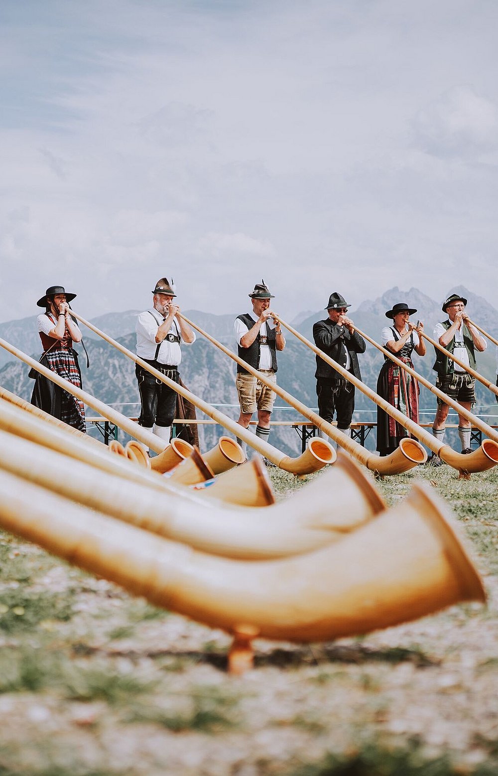 Männer und Frauen in Tracht spielen Alphorn auf einem Berg