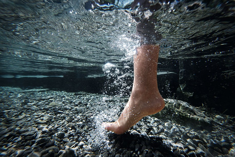 Ein Fuß im Wasser, am Boden Kieselsteine