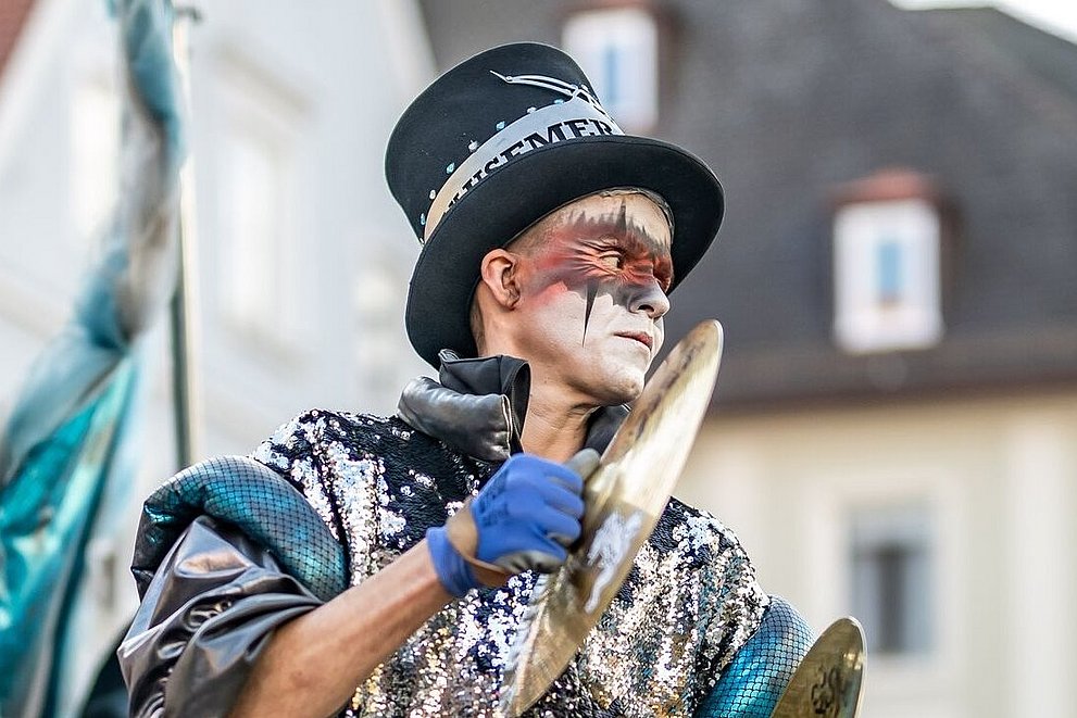 Verkleideter Guggenmusiker spielt Becken in der Memminger Altstadt
