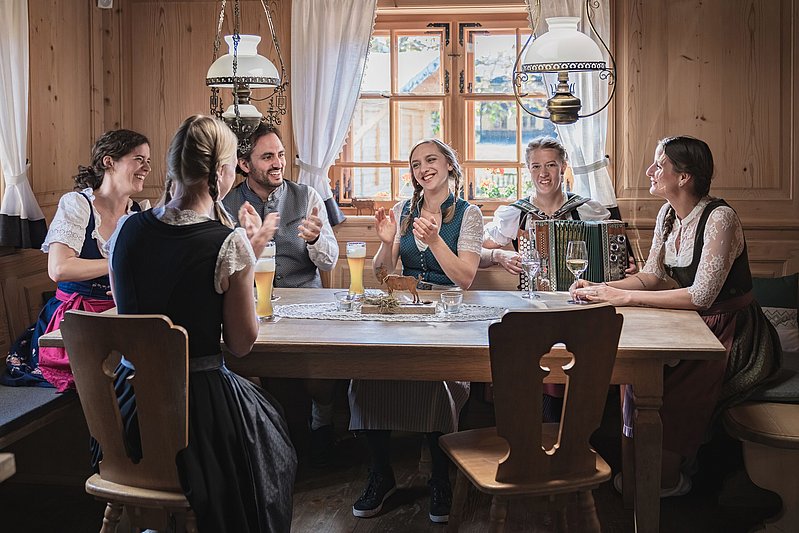 Gruppe in Tracht sitzt in einer Wirtschaft, einer spielt Ziehharmonika