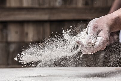 Gekonnt streut die Bäckershand Mehl auf die Arbeitsfläche