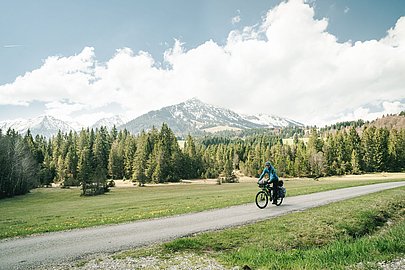 Radfahrer mit Gepäck auf der Radrunde bei Unterjoch, im Hintergrund Wiese, Wald und Berge