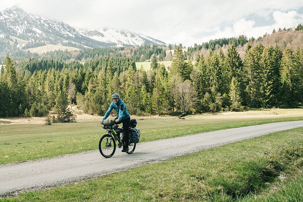 Radfahrer mit Gepäck auf der Radrunde bei Unterjoch, im Hintergrund Wiese, Wald und Berge