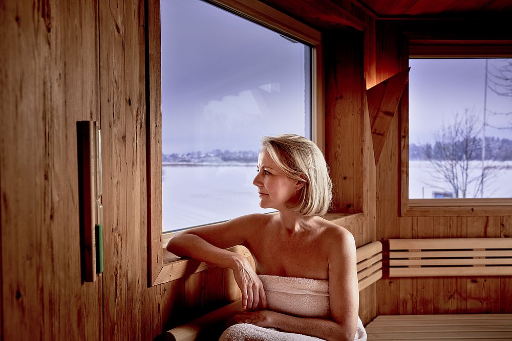 Frau in der Sauna des Hotel Sommer, verschneite Landschaft vor dem Fenster