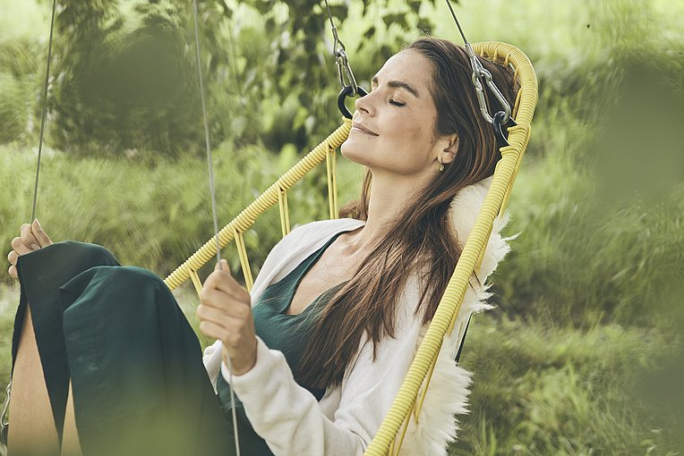 Frau mit geschlossenen Augen in einem Hängestuhl im Grünen