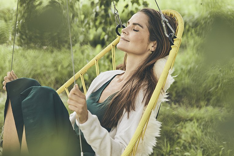 Frau mit geschlossenen Augen in einem Hängestuhl im Grünen