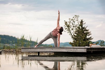 Frau macht Yoga auf einer Holzterrasse an einem See