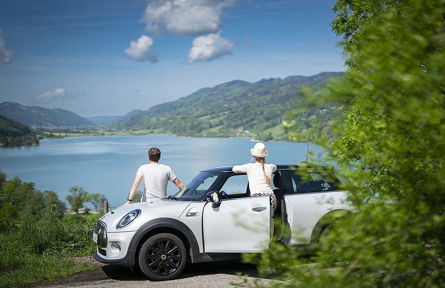 Ein Paar lehnt an einem Auto und genießt den Ausblick auf den Großen Alpsee