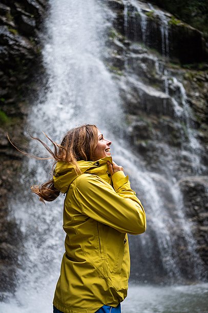 Frau mit wehendem Haar vor einem Wasserfall