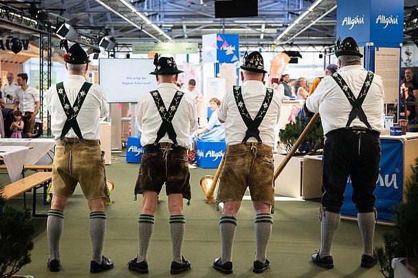Vier Männer in Tracht von hinten spielen Alphorn im Haus der Allgäuer Werte