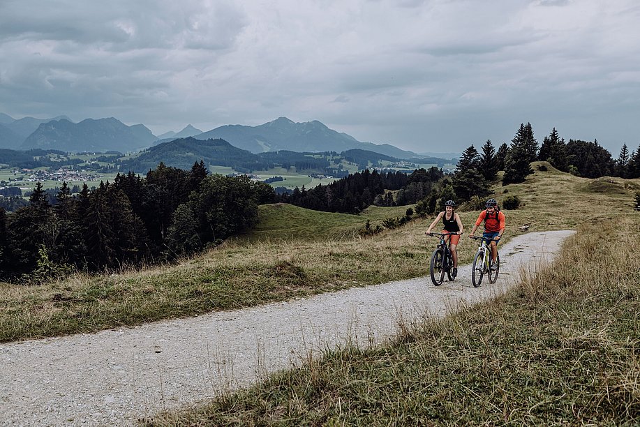 Zwei Radler auf einem Schotterweg, im Hintergrund die Berge