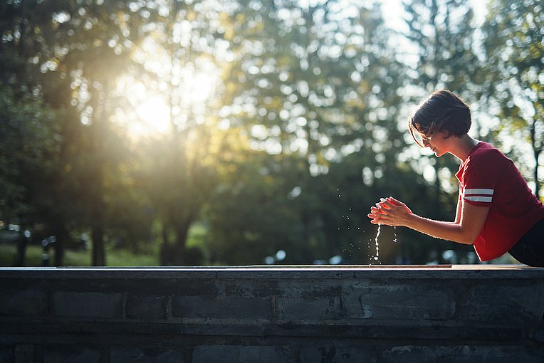 Frau an einem Kneippbecken, von den Armen tropft Wasser