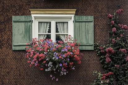Fenster mit Fensterläden und bunten Blumen an einem geschindelten Haus