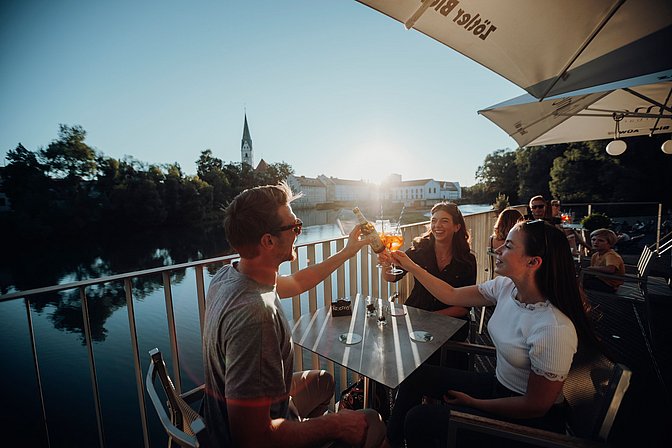 Eine Gruppe Menschen prostet sich bei Sonnenuntergang in der Fiume Sommerbar in Kempten zu