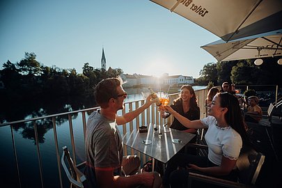 Eine Gruppe Menschen prostet sich bei Sonnenuntergang in der Fiume Sommerbar in Kempten zu