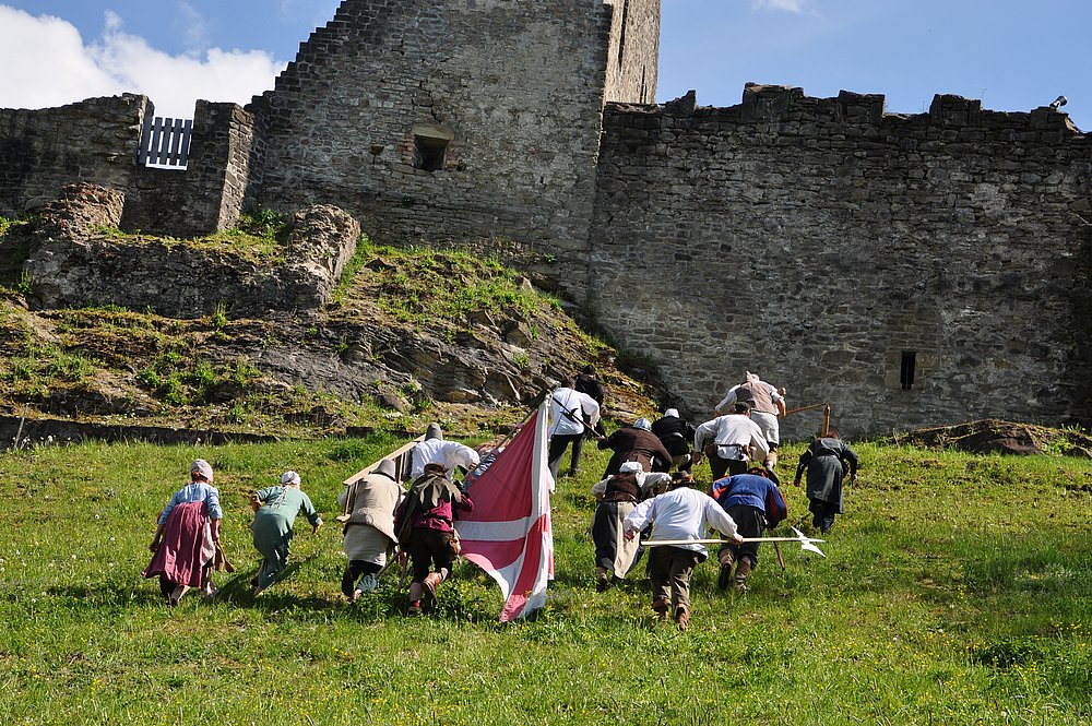 Menschen in mittelalterlicher Kleidung laufen hinauf zur Burg Sulzberg